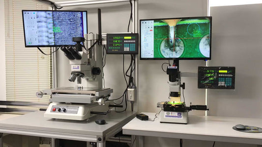 A high-precision optical inspection system featuring two microscopes with dual monitors and touch control panels on a white worktable in a lab setting.
