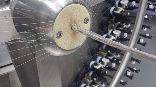 Close-up of a fine wire braid on mmbt 96 carrier horizontal braider with a beige circular cone head, silver metal components, and many thin threads radiating outward.